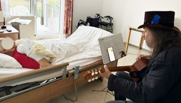 Liedermacher Daniel Fernholz besucht mit seiner Gitarre eine Bewohnerin in ihrem Zimmer und spielt Schlager. Foto: Bonmonde / Tamara Lieber