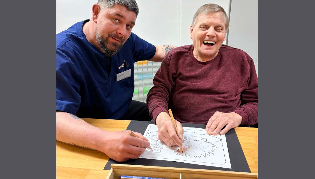 Betreuungskraft Daniel Rüffer unterstützt den Bewohner Friedrich-Wilhelm Buchholz beim Malen von Ostermotiven.
